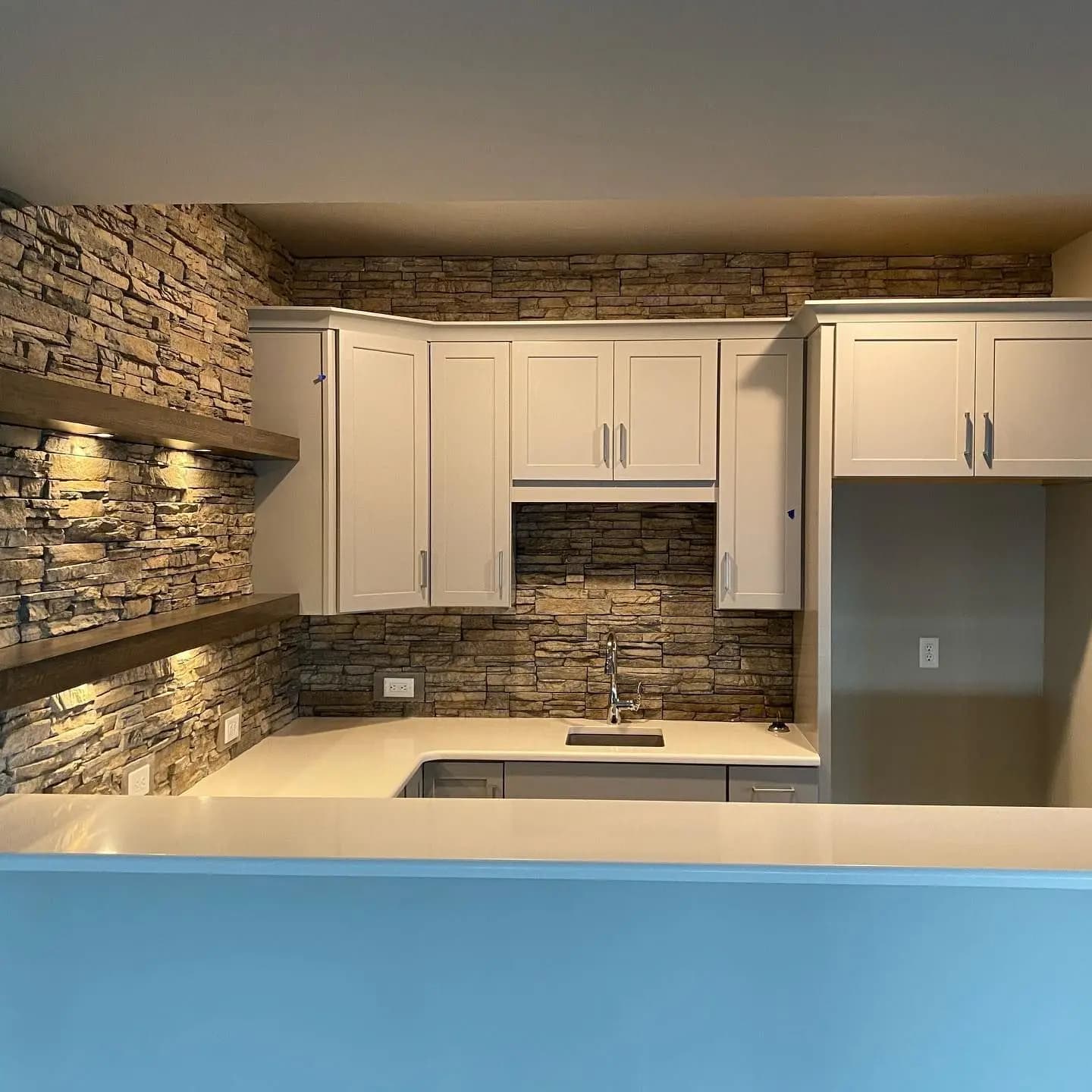 a kitchen with a stone wall and white cabinets